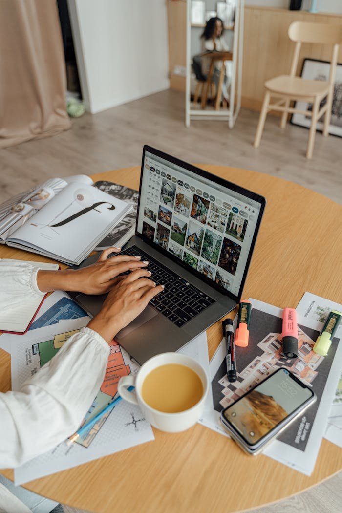 A person working from home with a laptop, coffee, and magazines on a wooden table, showcasing a freelancing lifestyle.